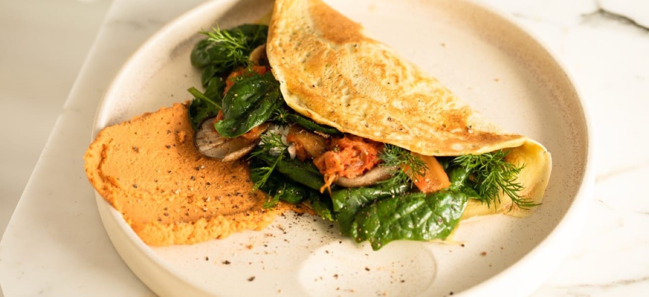 Omelette filled with various greens, tomatoes, and mushrooms on a plate